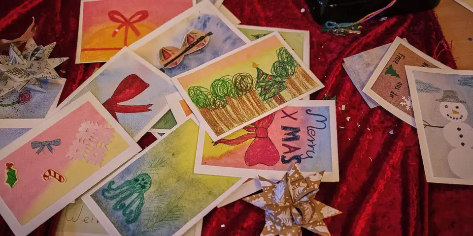 Handgemalte Weihnachtskarten liegen auf rotem Stoff.