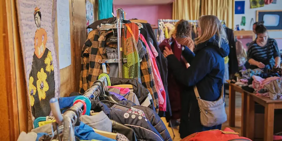 Menschen stöbern in einem Raum an Kleiderständern mit Secondhand-Kleidung.