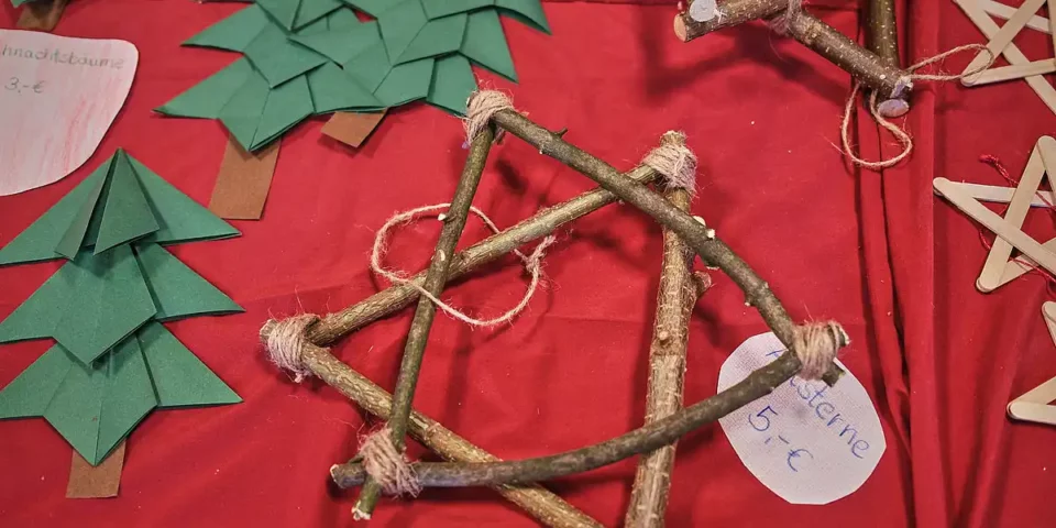 Handgemachte Weihnachtsdekoration aus Zweigen und Papierbäumen auf einem Tisch beim Adventsfest.