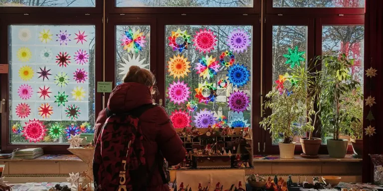 Eine Person betrachtet bunte Sternfenster und einen Adventsmarktstand im Innenraum der Rudolf-Steiner-Schule.