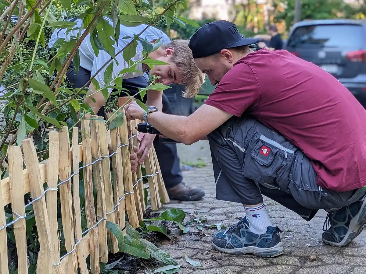 Zwei Personen bauen gemeinsam einen kleinen Holzzaun.
