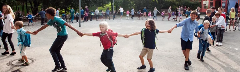 Kinder und Eltern bilden eine lange Schlange und gehen gemeinsam über den Schulhof.