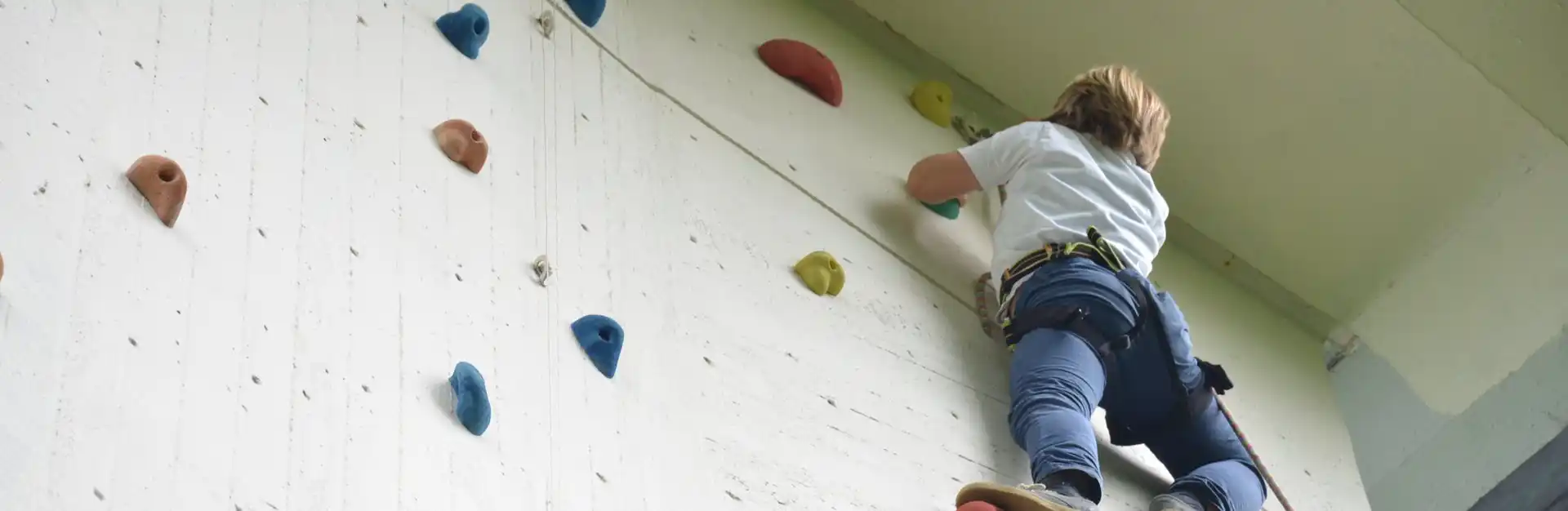Kind klettert an einer Kletterwand in der Turnhalle.