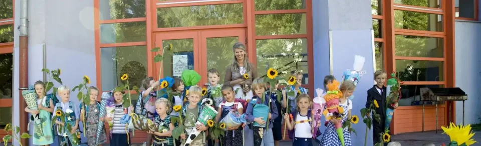 Erstklässler mit Schultüten und Sonnenblumen vor dem Schuleingang.