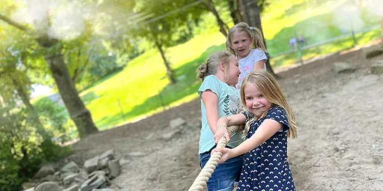 Drei Kinder spielen auf einem Spielplatz und ziehen gemeinsam an einem Seil.