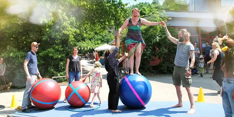 Person balanciert mit Unterstützung auf einem großen Zirkusball während einer Mitmach-Zirkusaktion auf dem Schulhof.