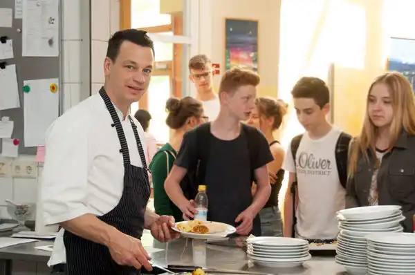Schülerinnen und Schüler holen Essen in der Schulküche ab.