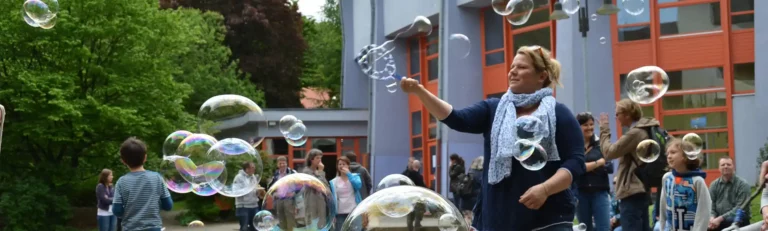 Kinder und Erwachsene machen gemeinsam große Seifenblasen auf dem Schulhof.