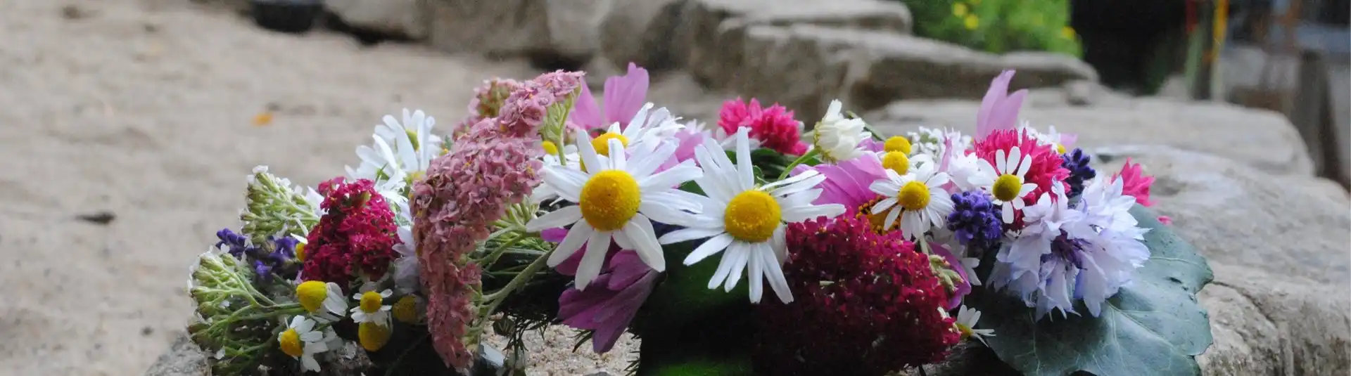 Blumenkranz aus Wiesenblumen liegt auf einem Stein.